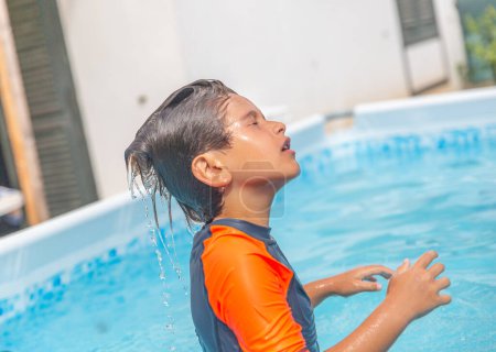Junge im Pool blickt nach oben, Wassertropfen strömen aus seinen Haaren und fangen den Geist des Sommers ein