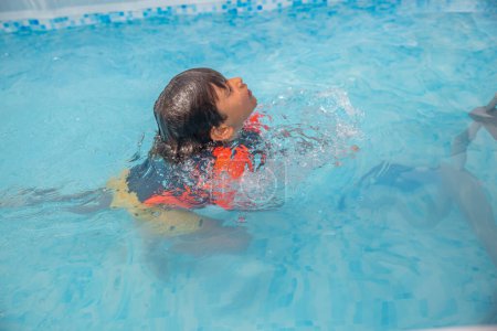 Young boy in vibrant orange and black swim gear relishing an underwater swim in a sunny pool