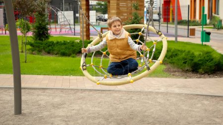 Photo for Smiling little boy rinding in rope web swing and having fun swinging. Active child, sports and development, kids playing outdoors. - Royalty Free Image