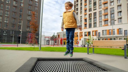 Téléchargez les photos : Joyeux garçon souriant sautant haut sur le trampoline extérieur à l'aire de jeux dans le parc. - en image libre de droit