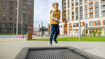 Téléchargez les photos : Joyeux petit garçon qui ressent joie et bonheur alors qu'il saute sur le trampoline dans la cour de l'école. Enfant actif, sport et développement, enfants jouant à l'extérieur. - en image libre de droit