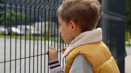 Photo for Portrait of upset little boy feeling alone looking through metal fence. Child depression, problems with bullying, victim in school, emigration, criminal and poverty. - Royalty Free Image