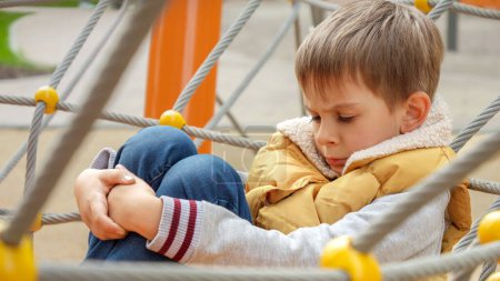 Téléchargez les photos : Portrait de petit garçon bouleversé assis seul sur le terrain de jeu et se sentant triste. - en image libre de droit