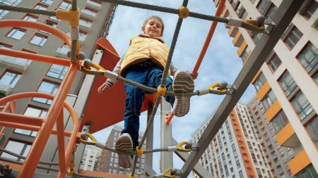 Photo for Happy smiling boy crossing the rope bridge on the playground at new city block. Active child, sports and development, kids playing outdoors. - Royalty Free Image