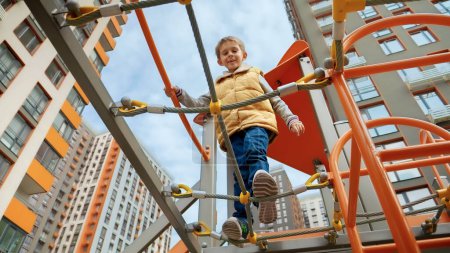 Photo for Little smiling boy crossing rope bridge between two towers on outdoor kids playground. - Royalty Free Image