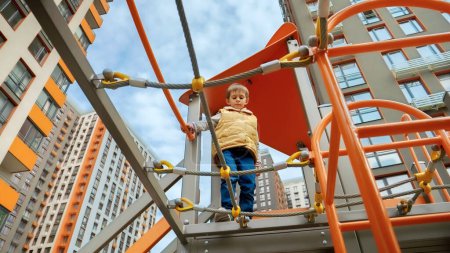 Photo for View from the ground on little boy walking over the rope bridge at playground. Active child, sports and development, kids playing outdoors. - Royalty Free Image