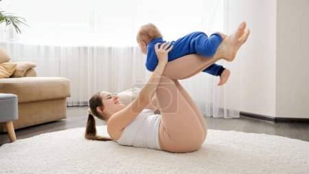 Photo for Happy young woman stretching on floor and playing with her baby son. Family healthcare, active lifestyle, parenting and child development. - Royalty Free Image