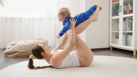 Téléchargez les photos : Joyeux petit garçon riant qui s'amuse avec sa mère faisant des exercices de fitness sur le sol. Santé familiale, mode de vie actif, rôle parental et développement de l'enfant. - en image libre de droit