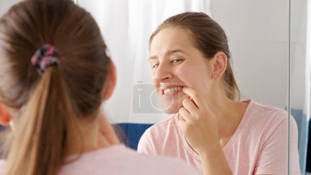 Téléchargez les photos : Portrait de jeune femme souriante ouvre la bouche et regarde le reflet de ses dents dans le miroir. Concept de santé dentaire, auto-contrôle de la bouche et hygiène buccale - en image libre de droit