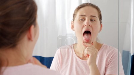 Porträt einer jungen brünetten Frau, die ihre Zunge im Spiegel auf Beläge und Mikroben überprüft.