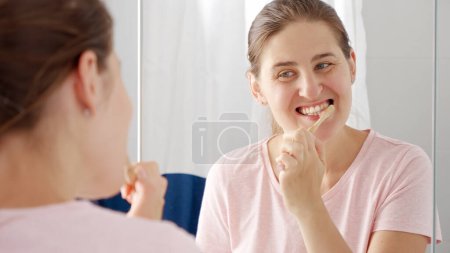Foto de Retrato de una joven sonriente lavándose los dientes por la mañana en el baño. Concepto de salud dental, autocontrol bucal e higiene bucal. - Imagen libre de derechos