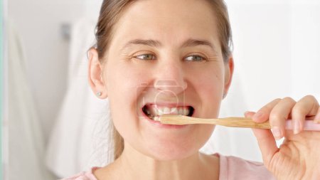 Foto de Fotografía en cámara lenta de una mujer joven cepillándose los dientes y mirándose en el espejo. Concepto de salud dental, autocontrol bucal e higiene bucal - Imagen libre de derechos