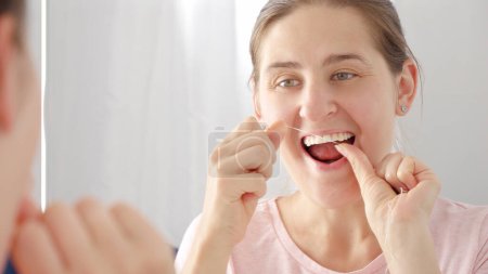 Téléchargez les photos : Portrait rapproché d'une jeune femme utilisant de la soie dentaire pour se laver les dents. Concept de santé dentaire, auto-contrôle de la bouche et hygiène buccale - en image libre de droit