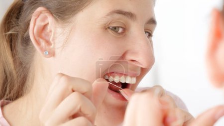 Téléchargez les photos : Une jeune femme utilisant de la soie dentaire pour nettoyer ses dents. Concept de santé dentaire, auto-contrôle de la bouche et hygiène buccale - en image libre de droit