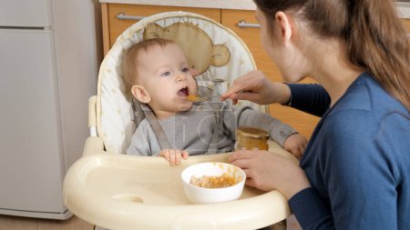 Foto de Happy little boy opens mouth for spoon with porridge. Concept of parenting, healthy nutrition and baby care - Imagen libre de derechos