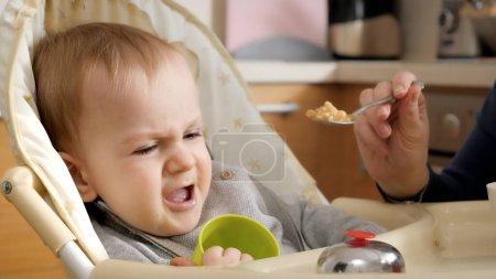 Photo for Portrait of angry screaming baby boy refusing eating food while sitting in highchair. - Royalty Free Image
