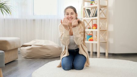 Photo for Happy smiling young woman calling her little baby boy learning walking on the carpet at living room. Baby development, making first steps, parenthood and care. - Royalty Free Image