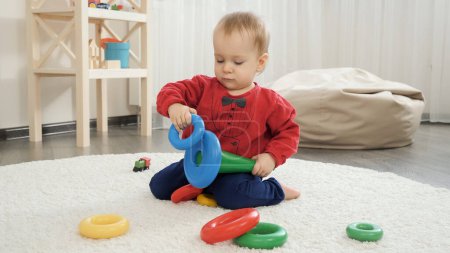 Photo for Cute little baby boy trying assembling colorful toy pyramid tower. Baby development, child playing games, education and learning - Royalty Free Image