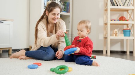 Téléchargez les photos : Joyeux babyboy avec mère jouant avec des jouets colorés sur le tapis dans le salon. - en image libre de droit
