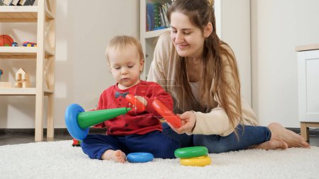 Photo for Cute little boy sitting with mother on carpet and playing with colorful toys. Baby development, child playing games, education and learning - Royalty Free Image