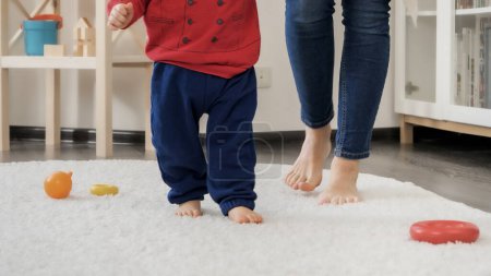 Photo for Closeup of little baby's feet learning walking with mother on soft carpet in living room. Baby development, family playing games, making first steps, parenthood and care. - Royalty Free Image