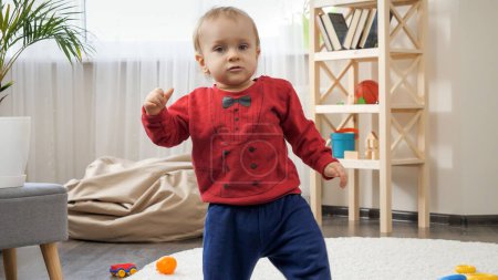 Photo for 1 year old baby boy standing up and making first steps on carpet in living room - Royalty Free Image