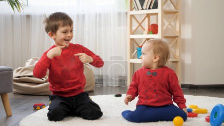 Téléchargez les photos : Drôle de plan de deux petits frères dansant sur le tapis dans le salon. Concept d'éducation des enfants, développement du bébé, famille s'amuser et jouer à des jeux - en image libre de droit