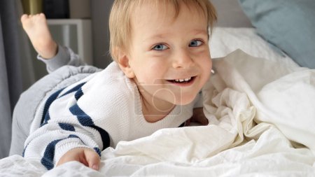 Téléchargez les photos : Joyeux garçon souriant tout-petit se détendre au lit le matin. Enfants heureux, se reposant à la maison - en image libre de droit