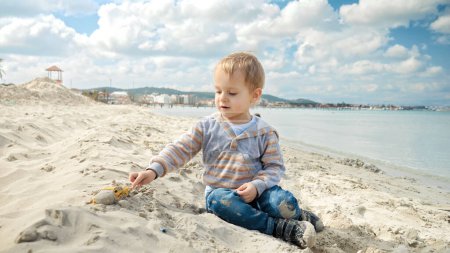 Foto de Un niño pequeño disfruta de un día relajante en la playa, jugando con la arena. Concepto de turismo, viajes, vacaciones de verano. - Imagen libre de derechos