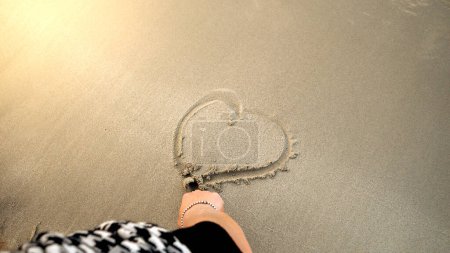 Foto de Primer plano de la mano femenina dibujando una forma de corazón de arena húmeda en la playa del mar. Concepto de viaje amoroso, consejos, viajes y turismo - Imagen libre de derechos