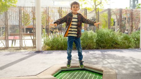 Téléchargez les photos : Mouvement lent du garçon heureux sautant haut sur le trampoline à l'aire de jeux pour enfants - en image libre de droit