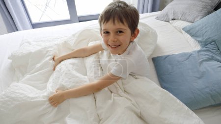 Téléchargez les photos : Petit garçon sautant de sous sa couverture avec un rire heureux et un grand sourire sur son visage, rayonnant un sentiment de pur plaisir et de plaisir - en image libre de droit