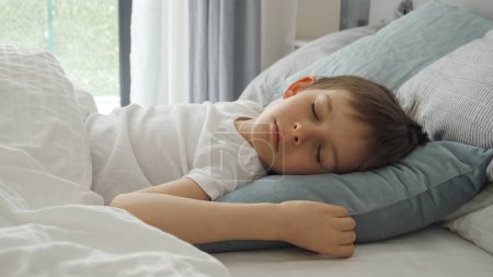 Téléchargez les photos : Gros plan du petit garçon dormant au lit près de la fenêtre le matin. Repos des enfants, soins de santé et relaxation des enfants. - en image libre de droit