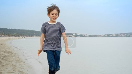 Photo for Happy smiling little boy runs and splashes the sea water. Travel, exploration, and the pursuit of fun and happiness - Royalty Free Image