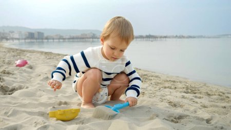 Photo for Adorable toddler boy happily playing with a shovel on the sandy beach. Represents the joy and fun of family travel, holidays, and vacations - Royalty Free Image