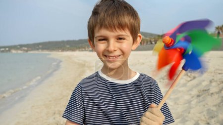 Photo for Portrait of cheerful smiling boy having fun on sea beach with colorful pinwheel. Concept of summer holiday, happiness, joy, travel and weekend - Royalty Free Image
