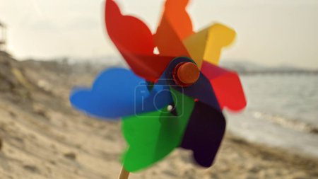 Foto de Colorido molinete gira alegremente en una playa de arena. La nostalgia de los veranos infantiles, el turismo de playa y la búsqueda de la felicidad - Imagen libre de derechos
