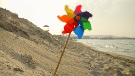 Foto de El viento sopla suavemente, un molinete gira en una playa de arena, capturando el espíritu de las vacaciones de verano, el turismo de playa y la aventura. - Imagen libre de derechos