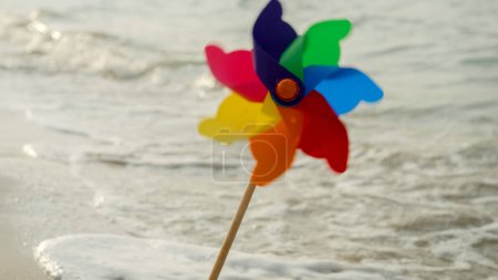 Foto de Colorido molinete gira en una playa de arena junto a las olas del mar, la alegría de viajar, la exploración, y la búsqueda de la felicidad y el cumplimiento - Imagen libre de derechos