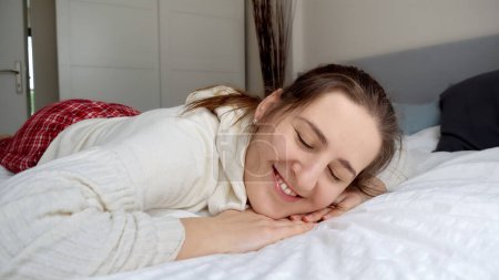Téléchargez les photos : Portrait d'une jeune femme joyeuse en pyjama couchée sur un lit doux. Concept de détente, de bonheur et de plaisir à la maison. - en image libre de droit