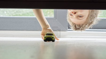 Photo for Little boy searching and taking his toy car lost under the bed. - Royalty Free Image
