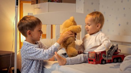 Téléchargez les photos : Deux garçons en pyjama jouant avec des jouets au lit avant d'aller dormir. Famille ayant du temps ensemble, parentalité, enfance heureuse et divertissement. - en image libre de droit