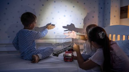 Téléchargez les photos : Enfants heureux avec mère jouant avec une lampe de poche dans le théâtre d'ombres la nuit. - en image libre de droit