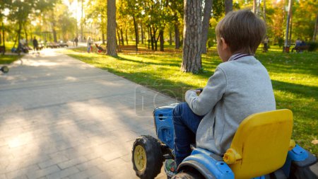 Téléchargez les photos : Petit garçon conduisant sur un tracteur électrique jouet dans le parc. Enfants jouant dans le parc, l'agriculture, le transport routier. - en image libre de droit