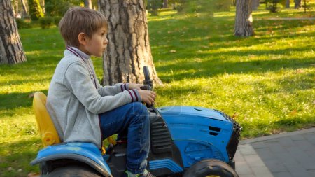 Téléchargez les photos : Joyeux garçon chevauchant sur tracteur jouet au parc. Enfants jouant dans le parc, l'agriculture, le transport routier. - en image libre de droit