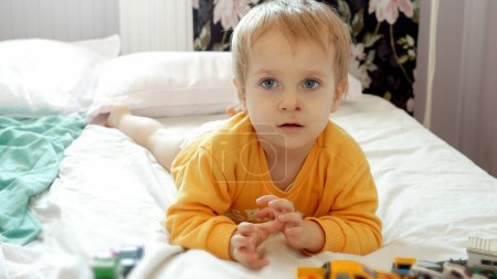 Photo for Cute funny boy with dirty face lying on bed and playing with colorful cars. Child development, education and entertainment. - Royalty Free Image