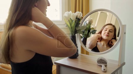 Téléchargez les photos : Jeune femme souriante assise au miroir rond et portant un pendentif en or. Mode, style féminin et beauté - en image libre de droit