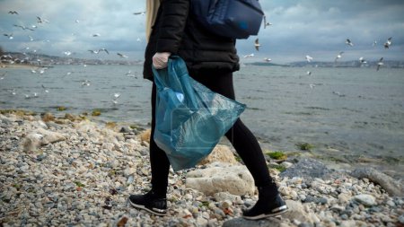 Foto de Mujer recogiendo basura en la playa con una bolsa de plástico, enfatizando la importancia de la conservación ambiental y la gestión de residuos - Imagen libre de derechos