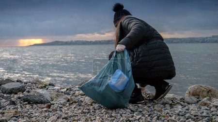 Photo for Young woman cleaning beach from garbage and trash and collecting all wastes in plastic bag. - Royalty Free Image