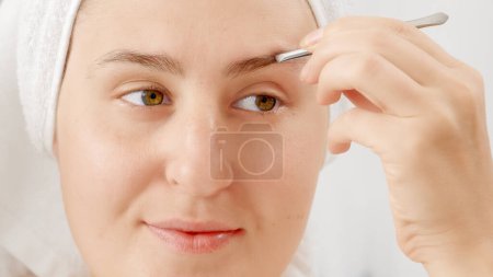 Photo for Young woman correcting shape of her yeybrows and plucking them in bathroom. Concept of beautiful female, makeup at home, skin care and domestic beauty industry - Royalty Free Image
